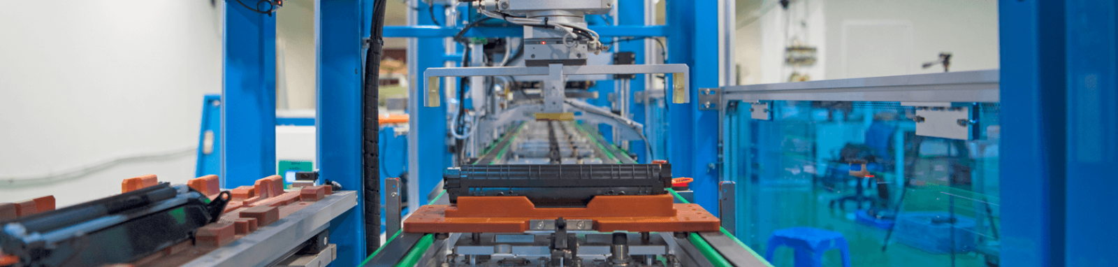 Maskin i fabrik som monterar produkter på löpande band, omgiven av blåa och orangea delar.